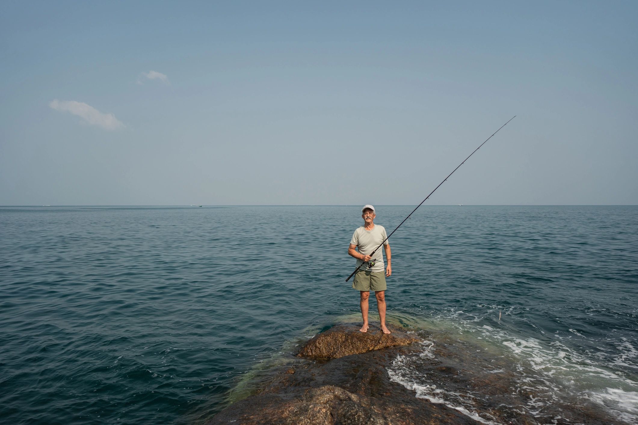 Senior fisherman holding a rod on a rocky shoreline